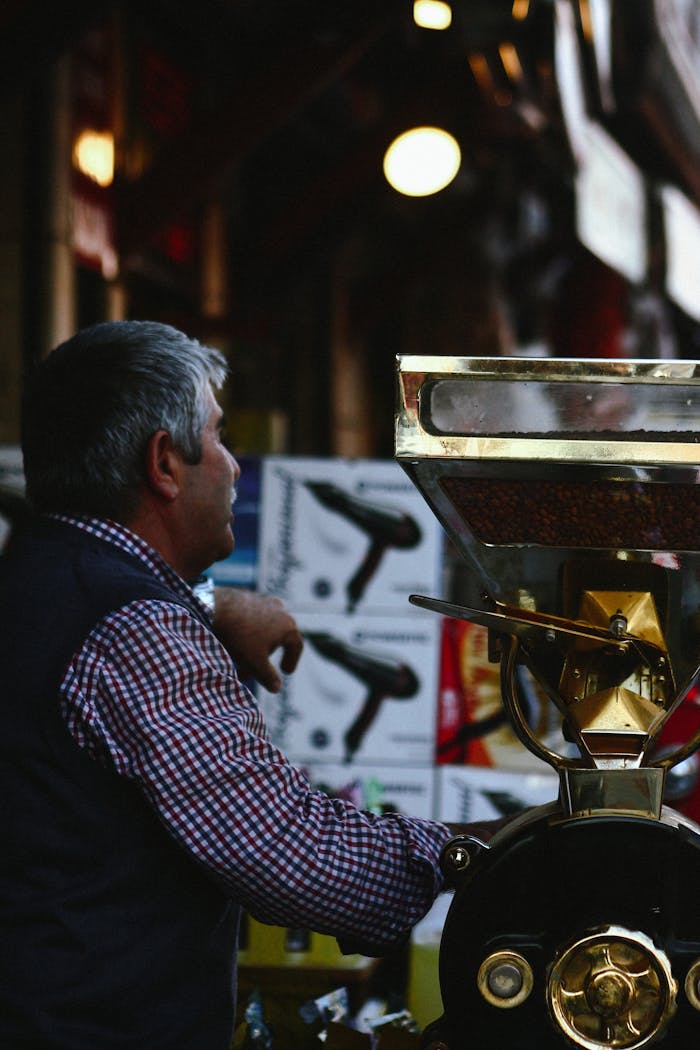 A man in a plaid shirt operates a large coffee grinder inside a bustling store.